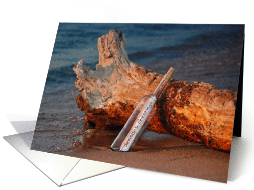 Season' Greetings message in a bottle with driftwood on a beach card