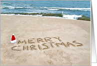 Merry Christmas in beach sand with Santa hat card