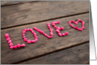 Love written with pink stones on a wooden table card