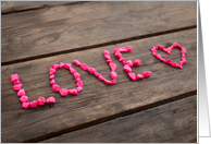 Love written with pink stones on a wooden table card